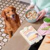 Verpakking Nutriment Fresh naast een gevulde voerbak op het aanrecht, met een wachtende hond ernaast
