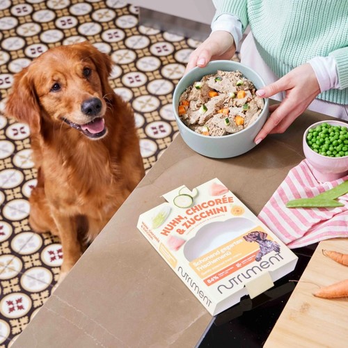 Verpakking Nutriment Fresh naast een gevulde voerbak op het aanrecht, met een wachtende hond ernaast
